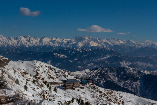 View of a snow dusted mountain range under a clear sky with a building nestled on the slope creating a serene yet rugged landscape Haveli Azad Kashmir Pakistan.
