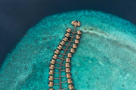 Aerial view of luxury overwater bungalows arranged along a curved wooden jetty over a vibrant turquoise coral reef and deep blue ocean water in Hoarafushi Haa Alif Atoll Maldives. Aerial view of luxury overwater bungalows arranged along a curved wooden jetty over a vibrant turquoise coral reef and deep blue ocean water in Hoarafushi Haa Alif Atoll Maldives.