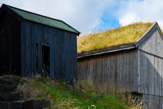 View of traditional wooden sheds with grass roofs set on a grassy hillside under a blue sky in the Faroe Islands. View of traditional wooden sheds with grass roofs set on a grassy hillside under a blue sky in the Faroe Islands.