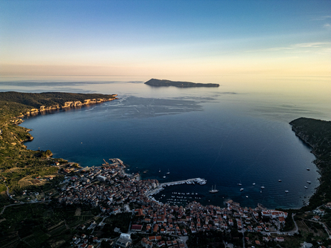 Aerial view of the coastal town of Komiza nestled in a deep bay with its harbor red roofed houses and the Adriatic Sea under a soft sunset sky in Komiza Split Dalmatia County Croatia.