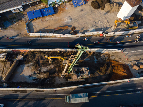 Aerial view of a construction site featuring a drilling rig and excavators working on earthwork near a busy road with traffic in Yogyakarta Special Region of Yogyakarta Indonesia. Aerial view of a construction site featuring a drilling rig and excavators working on earthwork near a busy road with traffic in Yogyakarta Special Region of Yogyakarta Indonesia.