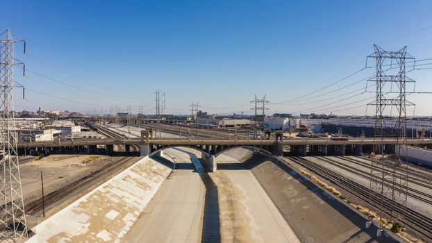 Aerial view of the Los Angeles River concrete channel with a bridge railway tracks and power transmission towers in the urban landscape of Los Angeles California United States.
