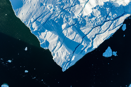 Aerial view of Ilulissat glacier featuring deep crevasses and intricate ice textures floating in the dark waters of Greenland. Aerial view of Ilulissat glacier featuring deep crevasses and intricate ice textures floating in the dark waters of Greenland.