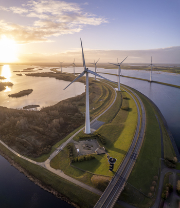 Aerial view of wind turbines standing along a dike and waterway during a golden sunset in the Netherlands. Aerial view of wind turbines standing along a dike and waterway during a golden sunset in the Netherlands.