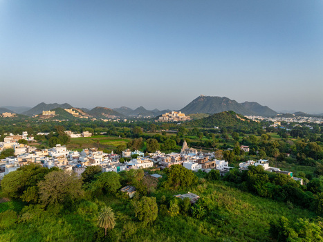 Aerial view of the historic city of Udaipur nestled among the Aravalli hills with white buildings lush green vegetation and distant mountain ranges in Udaipur Rajasthan India.