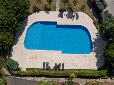 Aerial view of a blue swimming pool surrounded by a stone deck with lounge chairs and lush green hedges in Istanbul Istanbul Turkiye. Aerial view of a blue swimming pool surrounded by a stone deck with lounge chairs and lush green hedges in Istanbul Istanbul Turkiye.