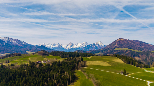 Aerial view of rolling green hills meeting the snow capped peaks under a bright blue sky streaked with contrails Windischgarsten Upper Austria Austria. Aerial view of rolling green hills meeting the snow capped peaks under a bright blue sky streaked with contrails Windischgarsten Upper Austria Austria.