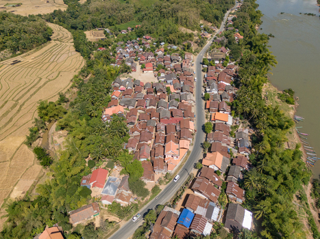 Aerial view of the village of Ban Hat Kho with traditional houses a winding road and terraced rice fields along the river in Ban Hat Kho Luang Prabang Province Laos.