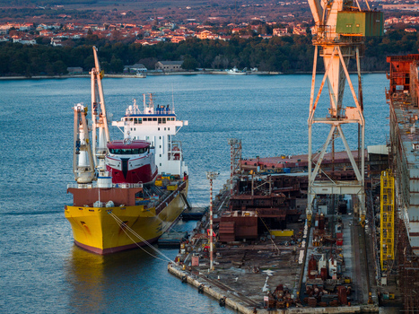 Aerial view of Uljanik Shipyard with a large yellow cargo ship docked at the pier industrial cranes and calm sea in Pula Croatia. Aerial view of Uljanik Shipyard with a large yellow cargo ship docked at the pier industrial cranes and calm sea in Pula Croatia.