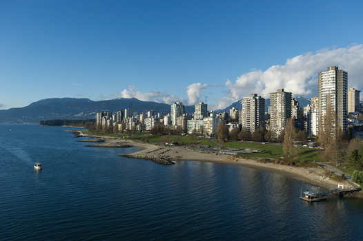 View of the Vancouver skyline along English Bay with high rise buildings sandy beach and mountains in the background in Canada.
