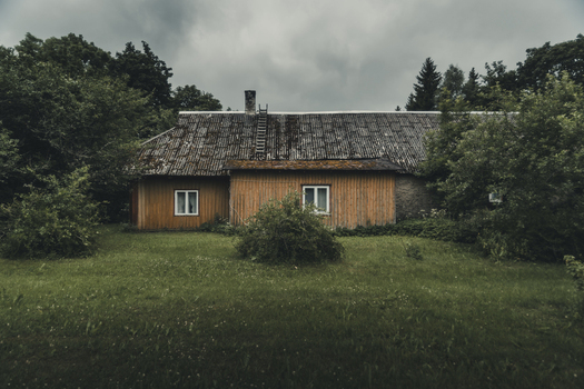 View of a traditional wooden house with a weathered roof surrounded by lush green trees and grass in Madise Harju County Estonia.