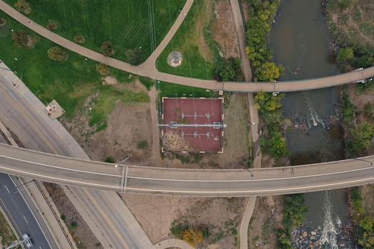 Aerial view of an electrical substation situated near a curved bridge a flowing river and park pathways in Denver Colorado United States. Aerial view of an electrical substation situated near a curved bridge a flowing river and park pathways in Denver Colorado United States.