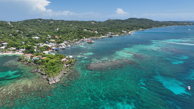 Aerial view of the coastline of West End featuring turquoise waters vibrant coral reefs lush green hills and buildings along the shore in West End Bay Islands Department Honduras. Aerial view of the coastline of West End featuring turquoise waters vibrant coral reefs lush green hills and buildings along the shore in West End Bay Islands Department Honduras.