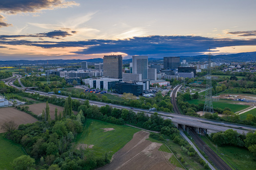 Aerial view of modern office buildings and skyscrapers surrounded by green fields and infrastructure under a sunset sky Eschborn Hessen Germany.