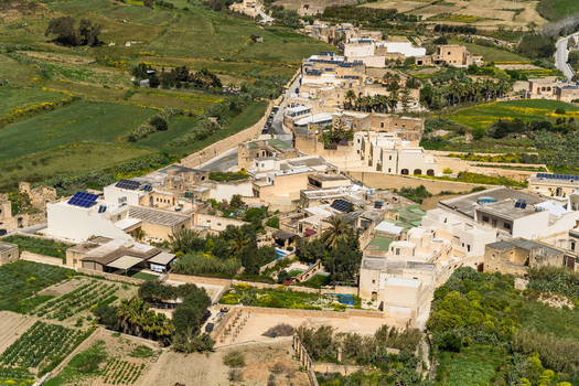View of traditional limestone houses with solar panels on rooftops overlooking lush green terraced fields and winding roads in the village of Zebbug Gozo Region Malta. View of traditional limestone houses with solar panels on rooftops overlooking lush green terraced fields and winding roads in the village of Zebbug Gozo Region Malta.