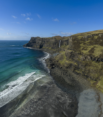 Aerial view of Talisker Bay Beach featuring rugged cliffs a waterfall and dark sand meeting turquoise waves on the Isle of Skye Scotland United Kingdom. Aerial view of Talisker Bay Beach featuring rugged cliffs a waterfall and dark sand meeting turquoise waves on the Isle of Skye Scotland United Kingdom.