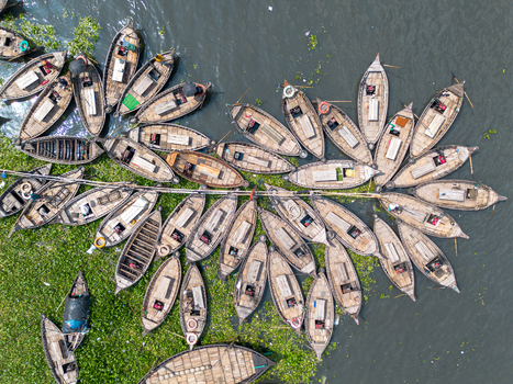 Aerial view of numerous wooden boats clustered on the Buriganga River with green water hyacinths and people in Dhaka Dhaka Division Bangladesh.