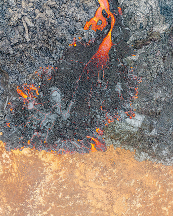 Aerial view of molten lava flowing over dark volcanic rock and barren earth in Iceland. Aerial view of molten lava flowing over dark volcanic rock and barren earth in Iceland.