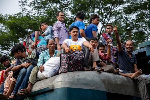 Dhaka Bangladesh 14 June 2018 View of people sitting on the roof of a train with their luggage at Airport Railway Station against a backdrop of green trees. Dhaka Bangladesh 14 June 2018 View of people sitting on the roof of a train with their luggage at Airport Railway Station against a backdrop of green trees.