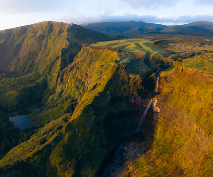Aerial view of Poco da Ribeira do Ferreiro waterfalls cascading down lush green cliffs into a valley during golden hour Fajazinha Azores Portugal. Aerial view of Poco da Ribeira do Ferreiro waterfalls cascading down lush green cliffs into a valley during golden hour Fajazinha Azores Portugal.