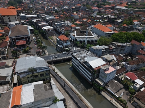 Aerial view of the dense urban landscape featuring a river a bridge with traffic and traditional orange tiled rooftops in Kecamatan Denpasar Barat Bali Indonesia. Aerial view of the dense urban landscape featuring a river a bridge with traffic and traditional orange tiled rooftops in Kecamatan Denpasar Barat Bali Indonesia.