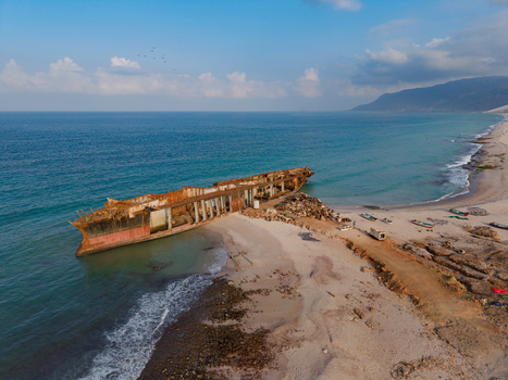 Aerial view of a rusted shipwreck beached on the sandy shore where the turquoise sea meets the rugged coastline Ararhin Yemen. Aerial view of a rusted shipwreck beached on the sandy shore where the turquoise sea meets the rugged coastline Ararhin Yemen.