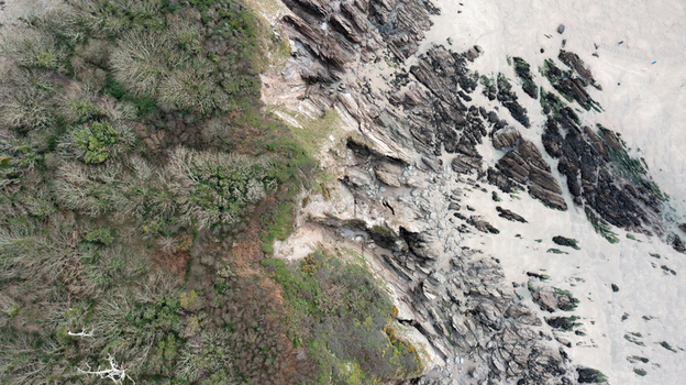 Aerial view of the rugged coastline featuring jagged rock formations a sandy beach and dense green woodland in Mothecombe Devon United Kingdom. Aerial view of the rugged coastline featuring jagged rock formations a sandy beach and dense green woodland in Mothecombe Devon United Kingdom.