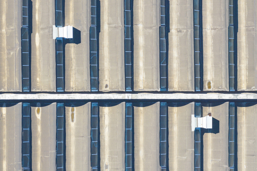Aerial view of industrial warehouse rooftops featuring corrugated metal panels long rectangular skylights and ventilation units in a geometric pattern in Arezzo Tuscany Italy. Aerial view of industrial warehouse rooftops featuring corrugated metal panels long rectangular skylights and ventilation units in a geometric pattern in Arezzo Tuscany Italy.