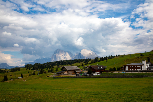 View of the Dolomites mountain range rising above traditional wooden huts in a lush alpine meadow under a dramatic cloudy sky in Rocca Pietore Veneto Italy. View of the Dolomites mountain range rising above traditional wooden huts in a lush alpine meadow under a dramatic cloudy sky in Rocca Pietore Veneto Italy.