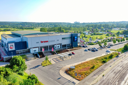 Bamberg Germany 02 May 2026 Aerial view of Brose Arena featuring its modern facade parking area and lush green surroundings under a bright clear sky.