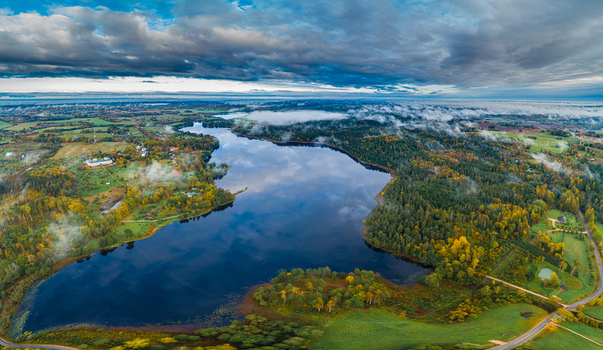 Aerial view of Araisi Windmill situated by the serene lake surrounded by vibrant autumn forests rolling fields and low hanging clouds in the countryside Drabesu pagasts Cesu novads Latvia. Aerial view of Araisi Windmill situated by the serene lake surrounded by vibrant autumn forests rolling fields and low hanging clouds in the countryside Drabesu pagasts Cesu novads Latvia.