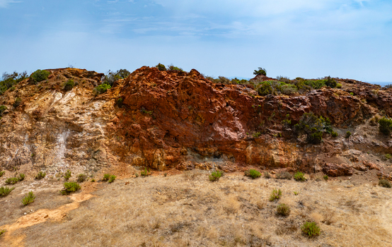Aerial view of the iron rich geological formations at the old iron mine area near Laghetto delle conche with reddish brown rock faces and sparse vegetation in Rio Marina Toscana Italy.