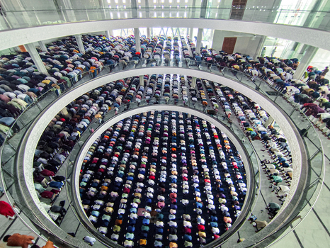 Dhaka Bangladesh 19 June 2026 Aerial view of a large congregation of men praying inside a modern mosque with circular balconies and patterned floors.