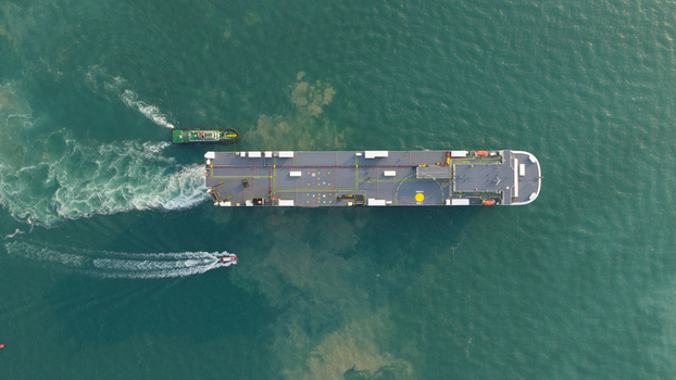 Aerial view of a large cargo ship and a tugboat navigating through turquoise waters with visible white wakes Laem Chabang Chon Buri Thailand.