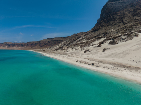 Aerial view of turquoise waters caress the sandy shores beneath rugged cliffs a serene landscape of contrasts Erissel Socotra Yemen.