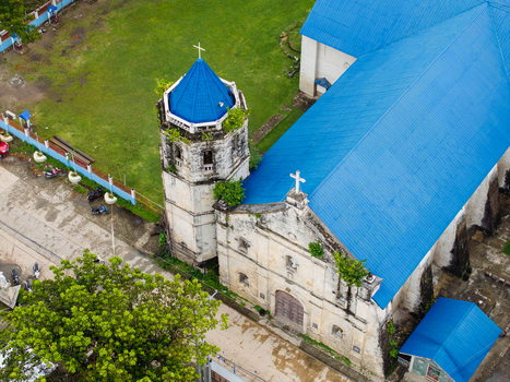 Aerial view of San Nicolas de Tolentino Parish featuring its distinctive blue roof and historic stone bell tower in Malabuyoc Central Visayas Philippines.