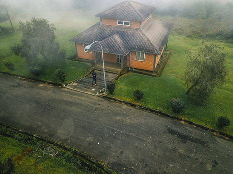 Aerial view of a vibrant orange roofed house emerging from misty green landscapes its steps leading to an empty road Obudu Cross River Nigeria.