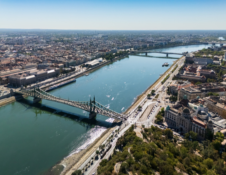 Aerial view of Liberty Bridge spanning the Danube beside dense historic cityscape and riverside streets in Budapest Hungary with Petofi Bridge in the distance on a sunny summer day. Aerial view of Liberty Bridge spanning the Danube beside dense historic cityscape and riverside streets in Budapest Hungary with Petofi Bridge in the distance on a sunny summer day.