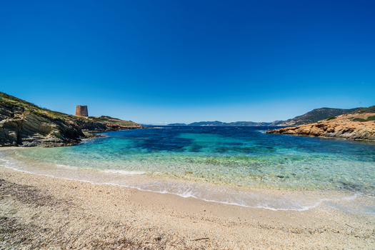 View of Spiaggia di Piscinni with turquoise water and the historic Torre di Piscinni tower on the rocky cliffs under a clear blue sky in Domus De Maria Sardegna Italy. View of Spiaggia di Piscinni with turquoise water and the historic Torre di Piscinni tower on the rocky cliffs under a clear blue sky in Domus De Maria Sardegna Italy.