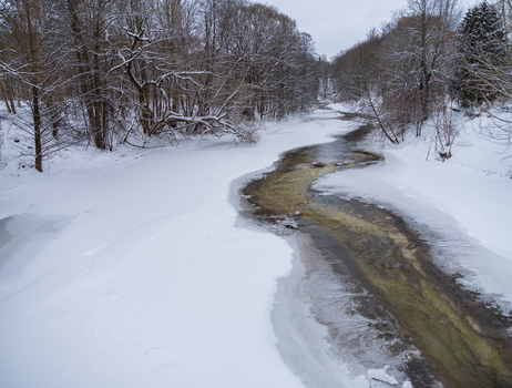 View of the partially frozen Vilnia River flowing through a snow covered forest in Vilnius Vilnius County Lithuania. View of the partially frozen Vilnia River flowing through a snow covered forest in Vilnius Vilnius County Lithuania.