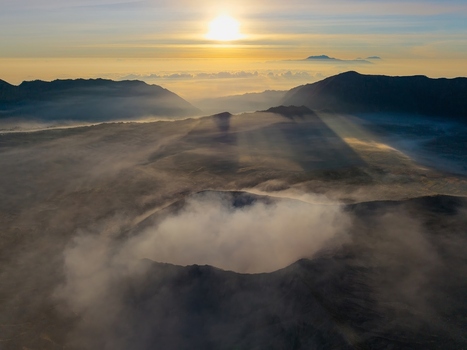 Aerial view of Mount Bromo sunrise with volcanic crater emitting smoke surrounded by misty mountains and dramatic sun rays at dawn in Tosari East Java Indonesia.