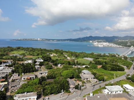 Aerial view of Sesoko Island connected by a bridge to the lush green coastline featuring residential houses dense vegetation and the blue sea in Motobu Okinawa Japan. Aerial view of Sesoko Island connected by a bridge to the lush green coastline featuring residential houses dense vegetation and the blue sea in Motobu Okinawa Japan.
