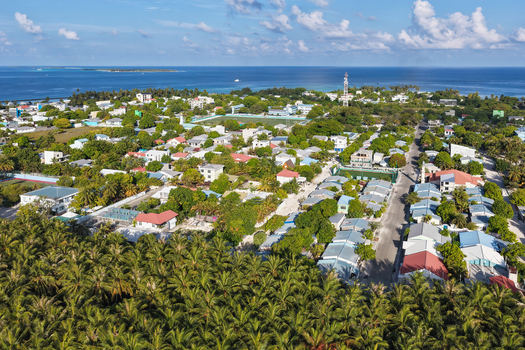 Aerial view of the island town featuring dense residential buildings lush palm trees and clear blue ocean surroundings in Kudahuvadhoo Dhaalu Atoll Maldives.