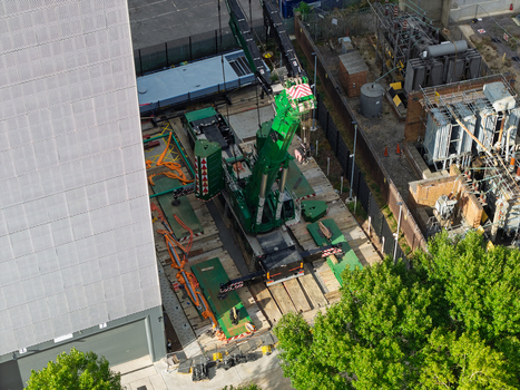 Aerial view of a green mobile crane positioned at a data center construction site featuring industrial equipment metal structures and surrounding green trees in the United Kingdom. Aerial view of a green mobile crane positioned at a data center construction site featuring industrial equipment metal structures and surrounding green trees in the United Kingdom.