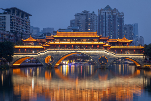 View of the illuminated Anshun Bridge reflecting in the Jin River with modern skyscrapers in the background in Chengdu Sichuan China.