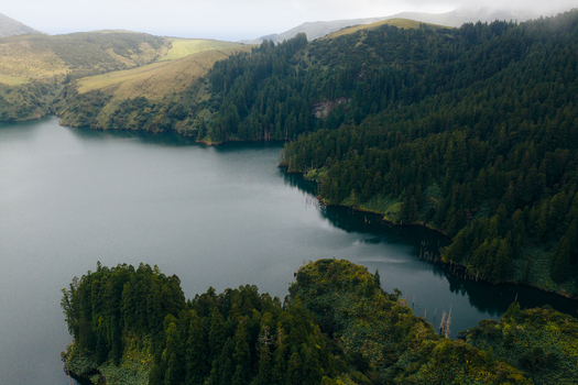 Aerial view of Caldeira Funda lake surrounded by lush green forests and rolling hills in Lajes das Flores Azores Portugal. Aerial view of Caldeira Funda lake surrounded by lush green forests and rolling hills in Lajes das Flores Azores Portugal.