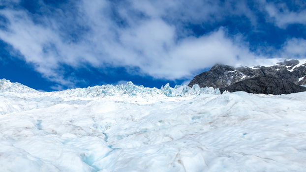 View of the glacier s icy expanse meets a rugged mountain under a bright sky with fluffy clouds creating a striking contrast Franz Josef West Coast Region New Zealand. View of the glacier s icy expanse meets a rugged mountain under a bright sky with fluffy clouds creating a striking contrast Franz Josef West Coast Region New Zealand.