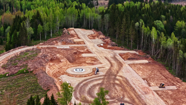 Aerial view of wind turbine foundation construction site with red soil heavy machinery tracks and surrounding dense pine forest in Latvia. Aerial view of wind turbine foundation construction site with red soil heavy machinery tracks and surrounding dense pine forest in Latvia.