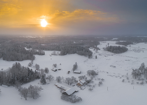 Aerial view of a snow covered rural landscape with farm buildings and trees during a golden sunset in Latvia. Aerial view of a snow covered rural landscape with farm buildings and trees during a golden sunset in Latvia.