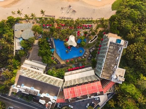 Aerial view of a luxury beach resort with a large blue swimming pool red umbrellas and lush palm trees bordering a sandy coastline in Galle Southern Province Sri Lanka.